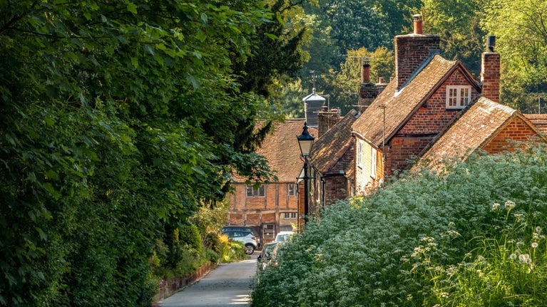 A view along Church Street in West Wycombe village showing old red brick houses in the distance and green bushes in the foreground